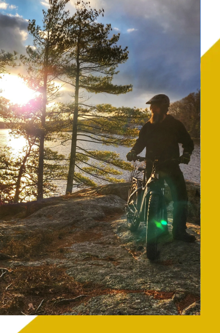 A man standing next to his bike on the side of a lake.