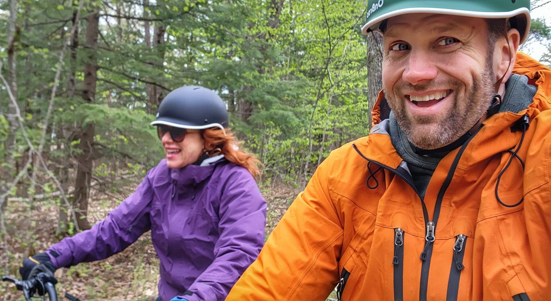 A man and woman riding bikes through the woods.