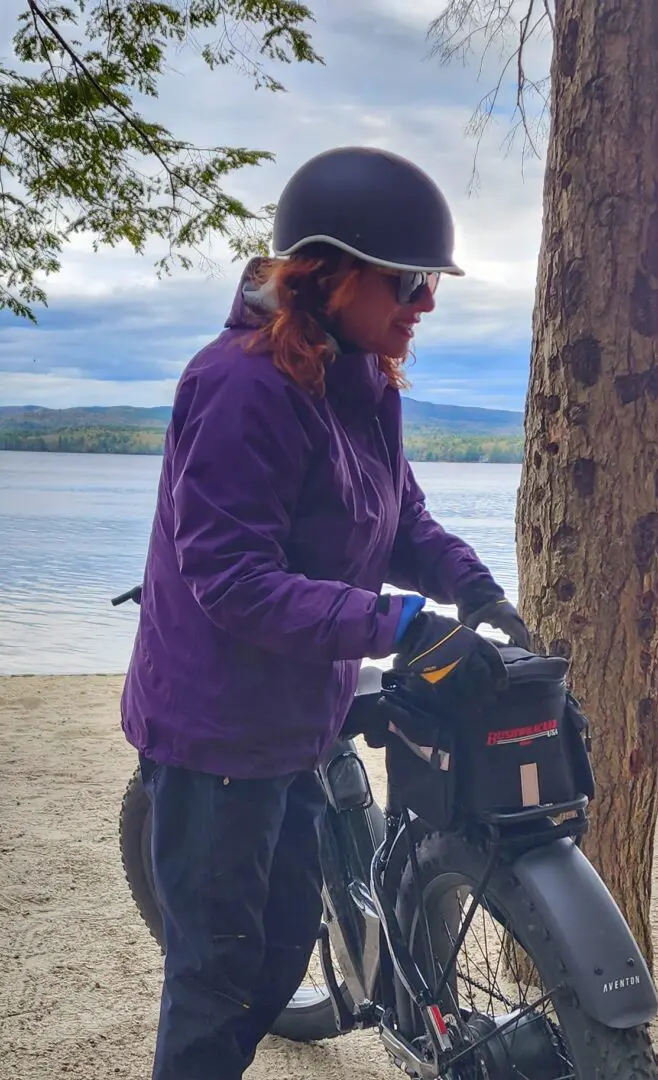 A woman in purple jacket standing next to tree.